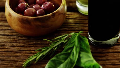 herbs and bowl of red olives on wooden table