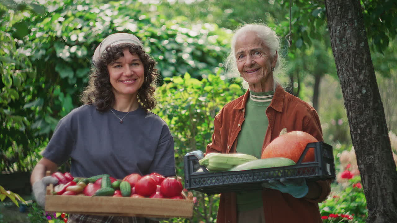 Smiling Women Holding Crates of Freshly Harvested Vegetables in Garden