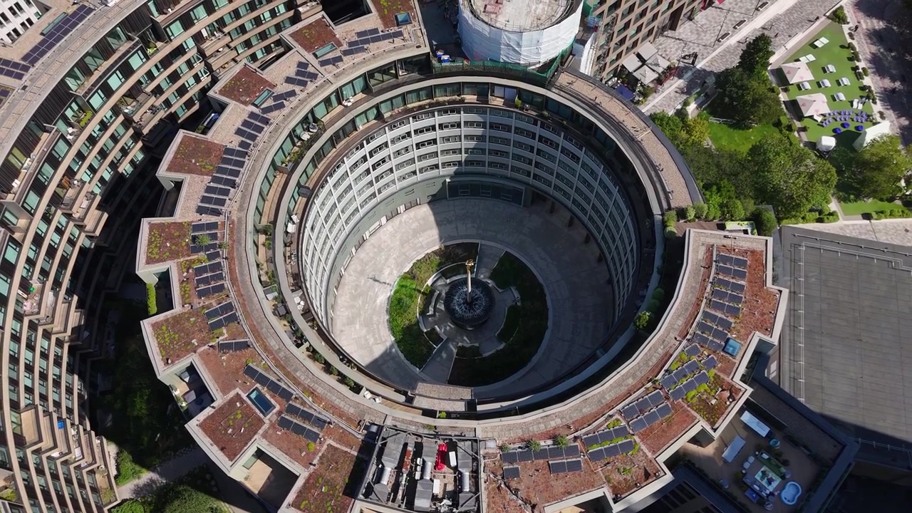 Edificio modernista circolare con un anello di balconi e terrazze sul tetto piantumate che racchiude un cortile pavimentato attorno a una fontana centrale.