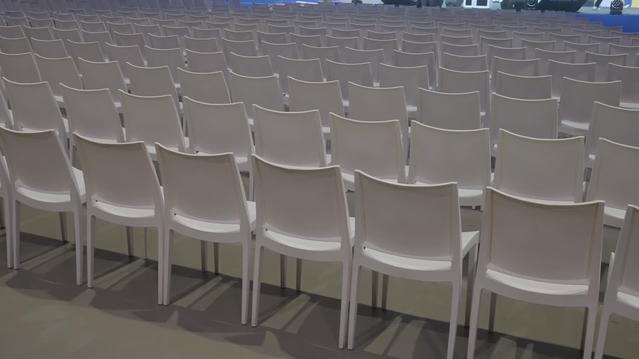 Empty white chairs arranged in rows inside an indoor event hall