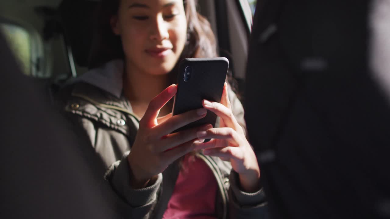 mujer asiática sonriendo mientras usa un teléfono inteligente mientras está sentada en el coche