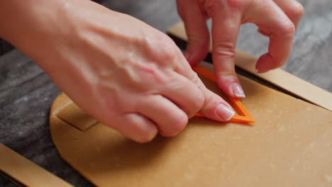 close-up of woman hands pressing orange cookie cutter into brown dough, creating precise shapes, manicured nails, baking preparation, textured countertop, wooden guides, and soft lighting