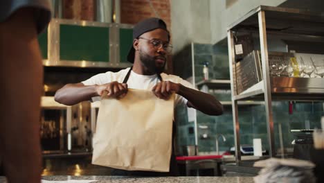 a black person serves a visitor in a doner market. a man puts an order to a customer in a paper bag. attention to the environment