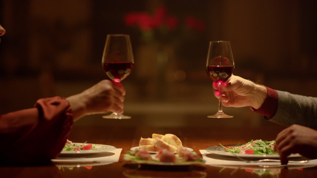 Primo piano: bicchieri di vino che tintinnano nelle mani di coppia anziana. Nonni che brindano.