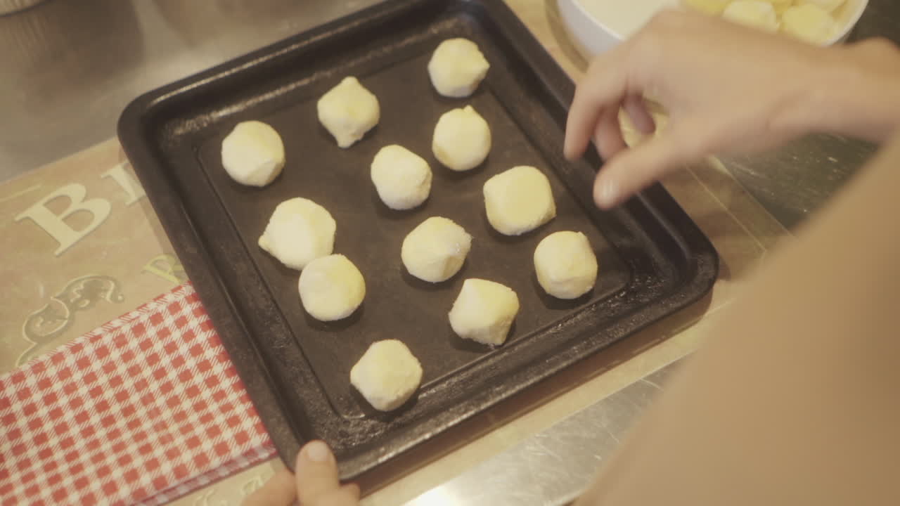 manos colocando cuidadosamente bolas de masa de chipa cruda en una bandeja de horneado, capturando el proceso de hacer pan sagrado tradicional en casa