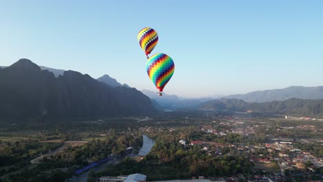 aerial-drone-shot-of-hot-air-balloons-above-the-river-in-Vang-Vieng,-the-adventure-capital-of-Laos