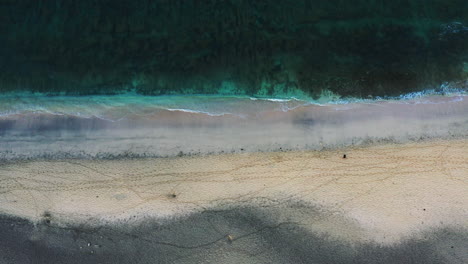 Aerial-top-down-shot-of-a-two-colored-sandy-beach-and-the-gentle-waves-with-a-person-slowly-walking-by-the-beach