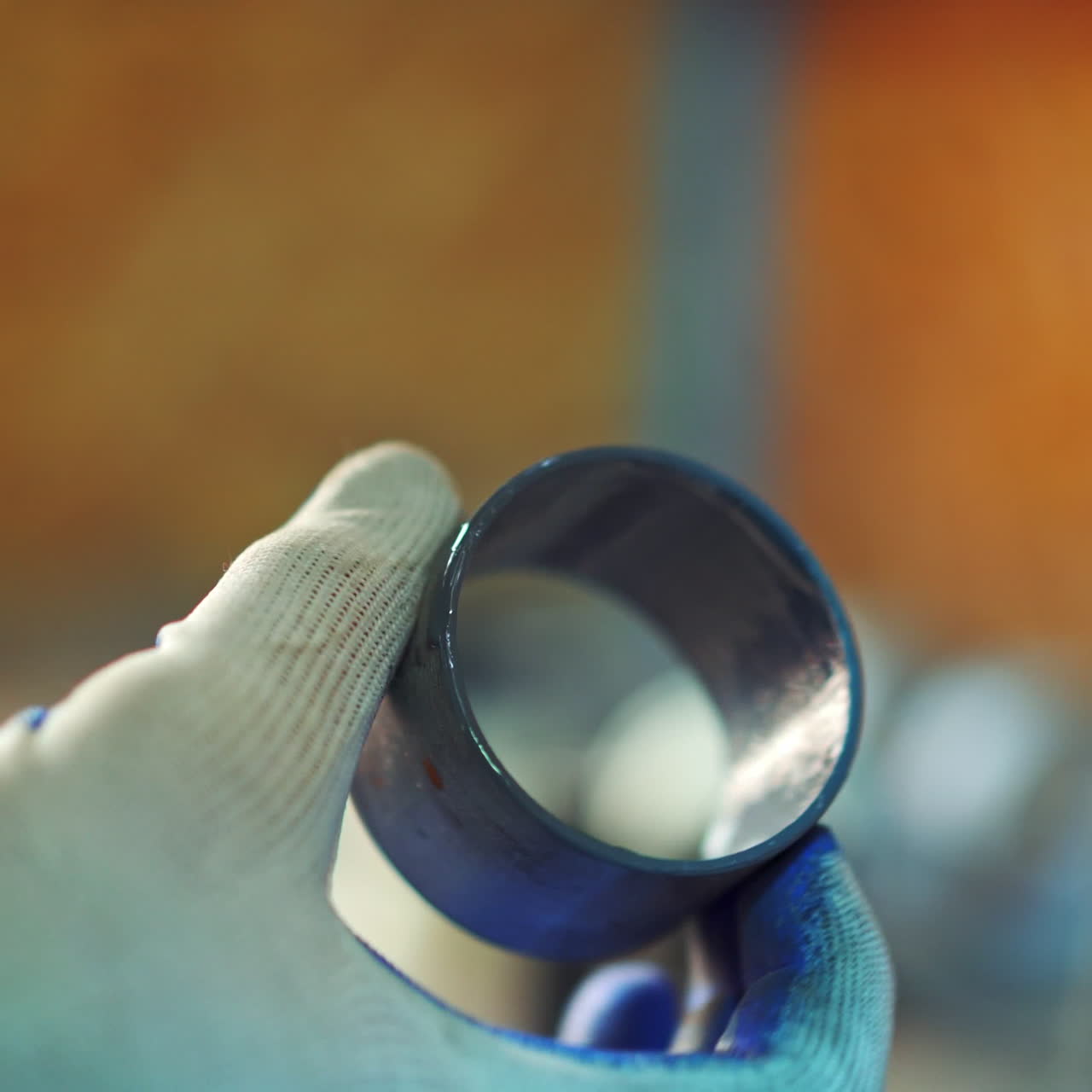 A worker is holding a ball bearing in his hand and coloring it with brush in blue colour on a blurred background. Close-up.