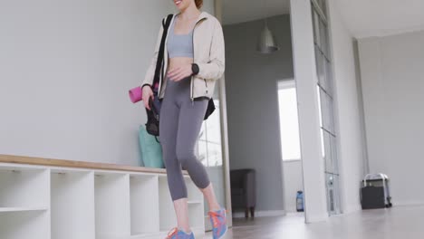 caucasian female ballet dancer entering a studio, smiling and sitting on a bench