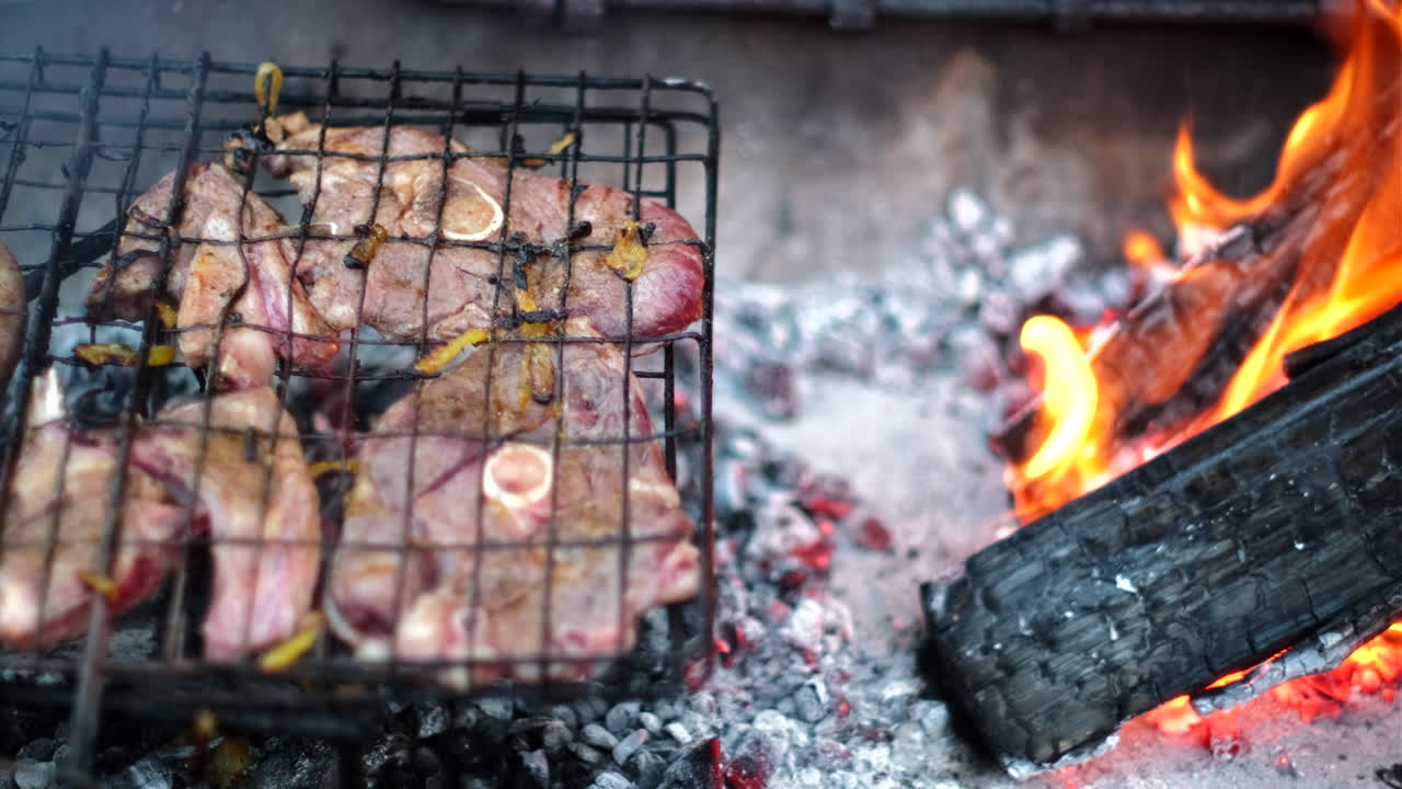 Mutton chops on grid being grilled on coals next to burning wood fire