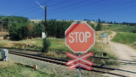 drone footage going up and above a stop sign by a railroad over train lines with dirt road and mountains in the background