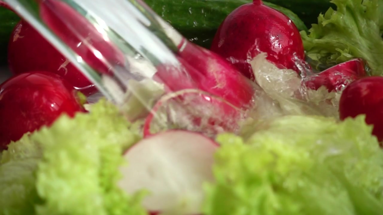 Radish, cucumbers and lettuce leaves in a stream of water. Slow motion.