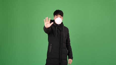 asian man in protective mask showing stop sign on a green screen