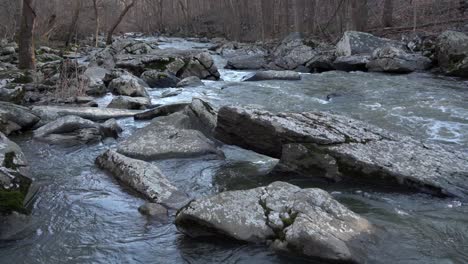 a river running over the rocks and boulders in the forest in the autumn season