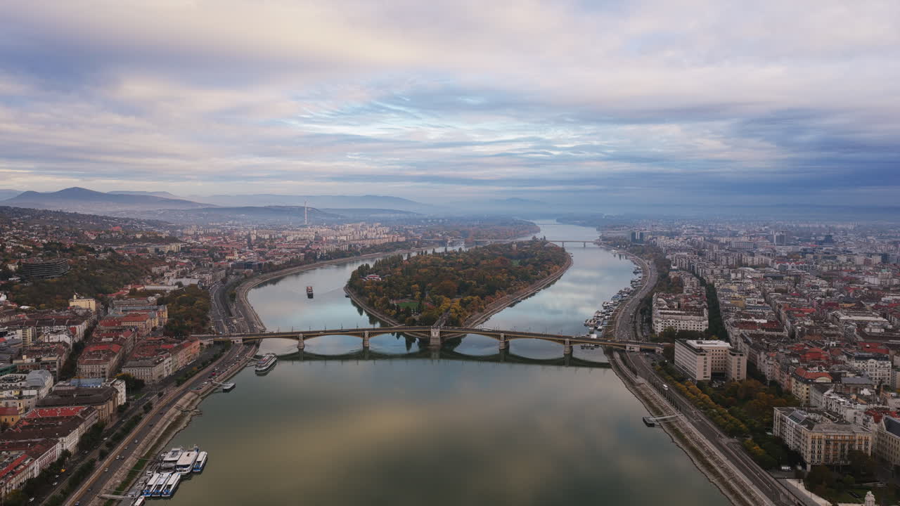 Aerial view of Margaret Island surrounded by the Danube, framed by Budapest’s historic architecture and misty hills