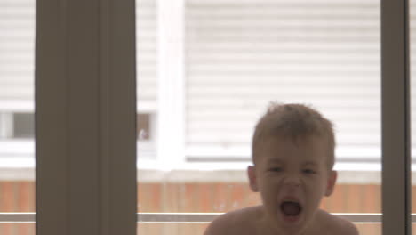 funny kid fooling with towel and having fun view through the glass