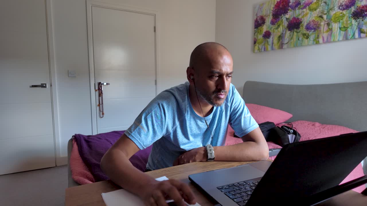Focused south asian freelancer working from home in his bedroom using laptop computer