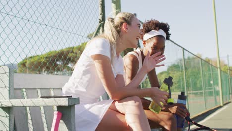 Video-of-happy-diverse-female-tennis-players-sitting,-talking-and-resting-after-match