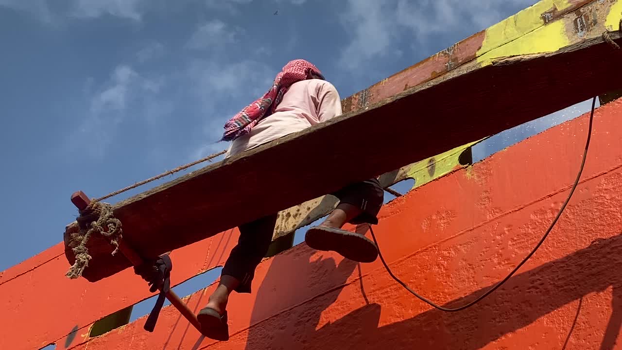 sylhet에 있는 나무 판자에 쉬고 있는 선박 선체에서 작업하는 작업자의 낮은 샷