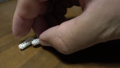 a hand picking up a pair of medicine capsules with pellets inside