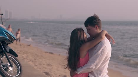 tall strong man hugs beautiful young lady on sandy beach