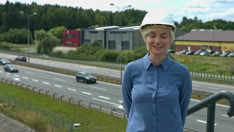 Frau-Auf-Der-Baustelle-Mit-Schutzhelm,-Die-Mit-Einem-Breiten-Lächeln-über-Einer-Autobahn-Steht