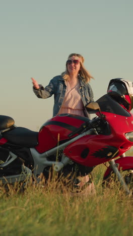 dos mujeres alegres están bailando cerca de una motocicleta roja en un campo de hierba bajo el cielo despejado, una de ellas sostiene un paño de limpieza mientras celebran y disfrutan de su tiempo al aire libre