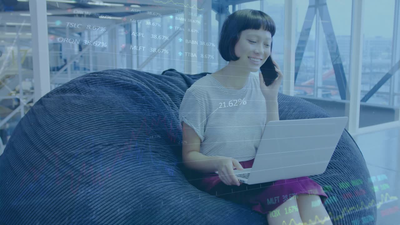 Woman taking call and typing on laptop with finance charts appearing around screen for data review