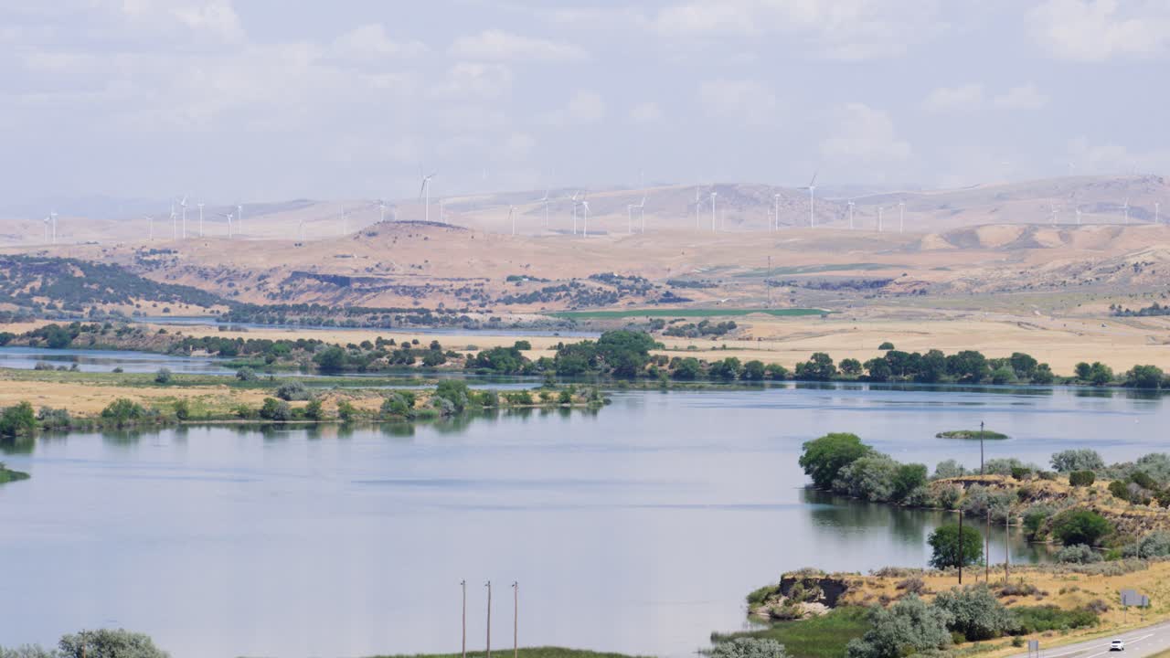 una toma amplia del río snake en idaho con turbinas eólicas girando en la distancia en un día de verano muy caluroso