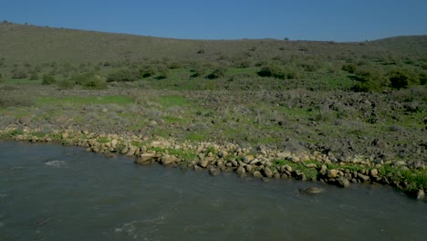 Ein-Wunderschöner-Blick-Auf-Die-Natur,-Der-Den-Jordan-Fluss-Zeigt,-Umgeben-Von-Kargen-Hügeln-Und-Felsigem-Gelände-Unter-Einem-Ruhigen-Blauen-Himmel