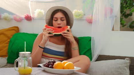 young woman eating fresh watermelon in backyard tent