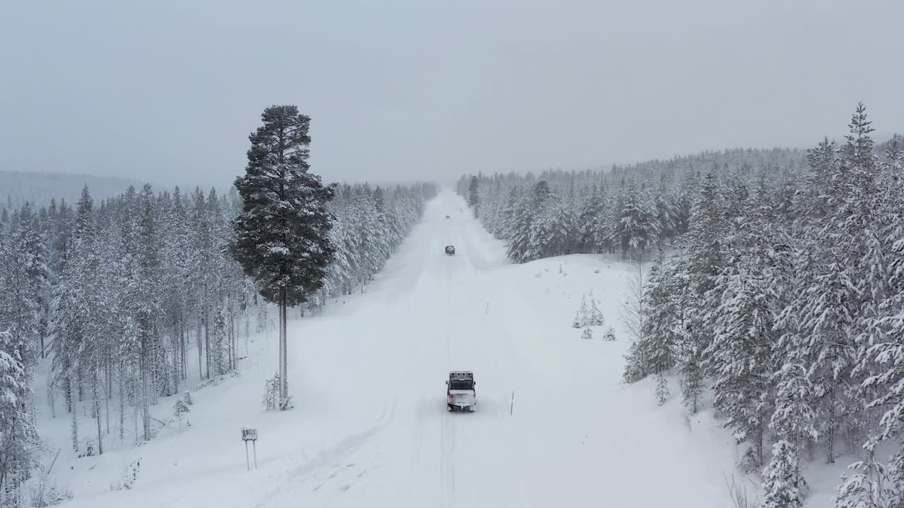 Aerial shot of cars driving on a snow covered road in Lapland during winter. Low to high angle shot.