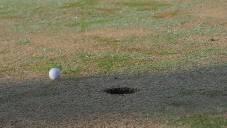 Geputteter-Golfball-Auf-Dem-Grün-Rollt-Am-Loch-Vorbei,-Niedrige-Und-Langsame-Bewegung