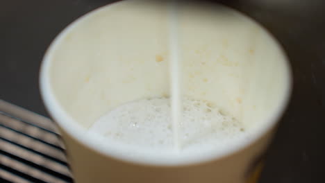 close view of milk being poured into a coffee cup from a coffee machine. the video captures the precise moment of the milk stream hitting the cup, emphasizing the details of the frothy milk