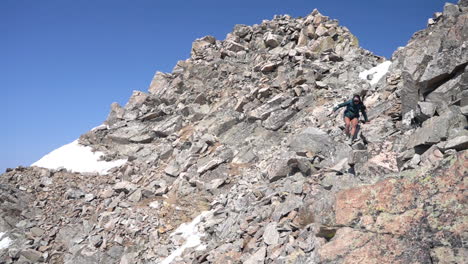 young female on rocky hillside heading downhill after climbing on top of summit on sunny day, slow motion