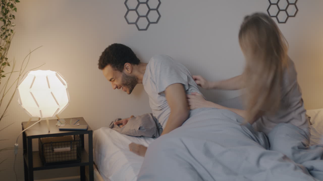 Couple having a playful pillow fight in bed at night