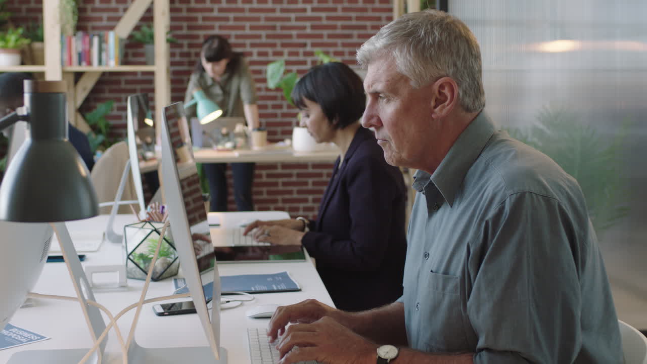 empresario caucásico senior usando computadora tormenta de ideas trabajando con diversos colegas ocupados en el espacio de trabajo de la oficina moderna