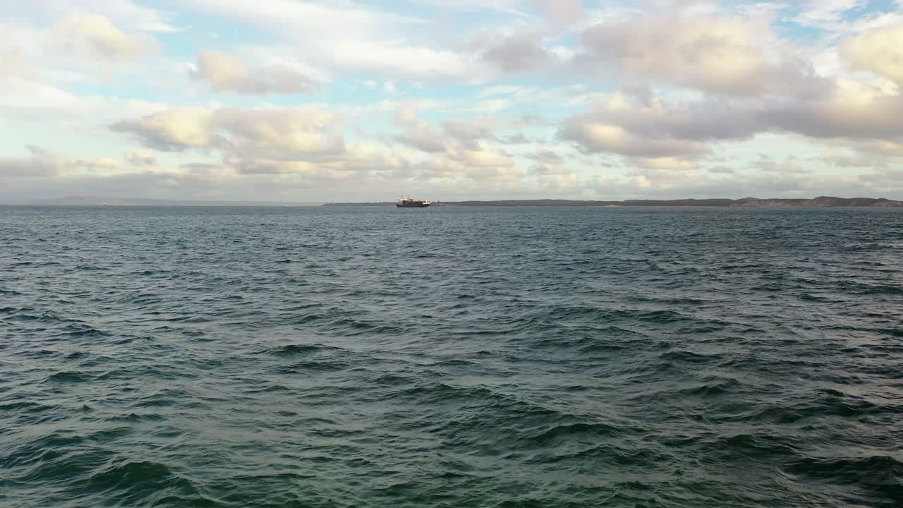 멀리서 컨테이너선을 향해 고르지 못한 물 위의 낮은 공중, 구름