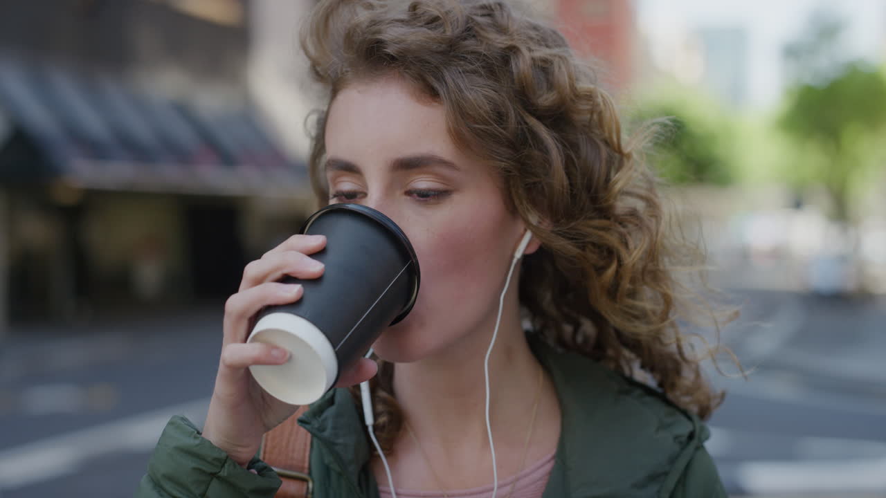 retrato de una hermosa mujer joven bebiendo café en la calle de la ciudad esperando una hermosa estudiante caucásica mirando a la cámara con auriculares