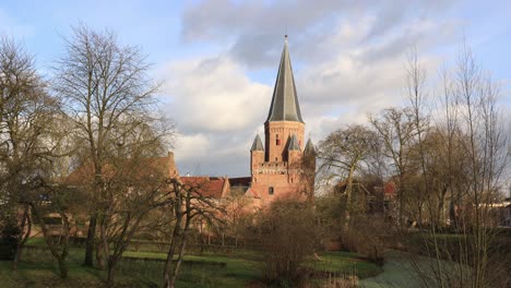 Stimmungsvoller-Blick-Auf-Den-Schützenden-Kanal-Vor-Der-Mittelalterlichen-Stadtmauer-Mit-Dem-Drogenapstoren,-Der-Sich-über-Der-Holländischen-Hansestadt-Zutphen-In-Den-Niederlanden-Erhebt,-Mit-Langsam-Vorbeiziehenden-Wolken