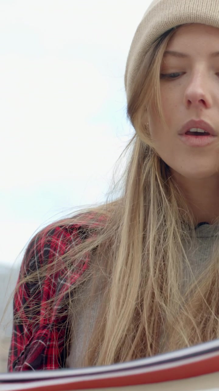 Vertical video: Panning camera showing woman studying notes on roof in beanie and plaid, copy space