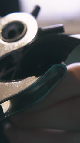 cu: skilled tailor makes holes in fashionable leather belt with special punch pliers in workshop extreme close view