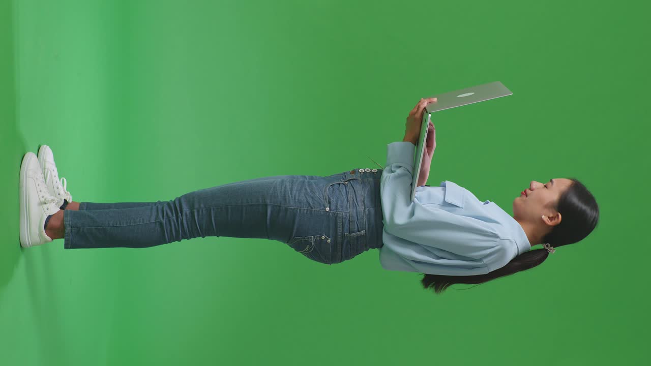 vista lateral de todo el cuerpo mujer de negocios asiática no está satisfecha y sacude la cabeza mientras usa la computadora portátil en el estudio de pantalla verde