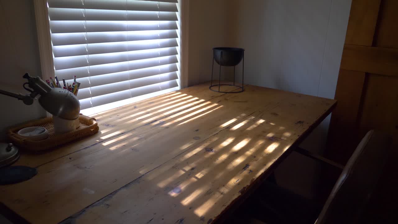 Relaxing sunrise sunlight rays fall through blinds onto a peaceful gorgeous wooden desk and leather chair. Perfect office workspace for anyone. 4k slow motion shot