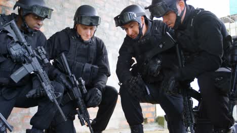 side view of mixed-race military soldiers with rifles planning and crouching on floor at base 4k