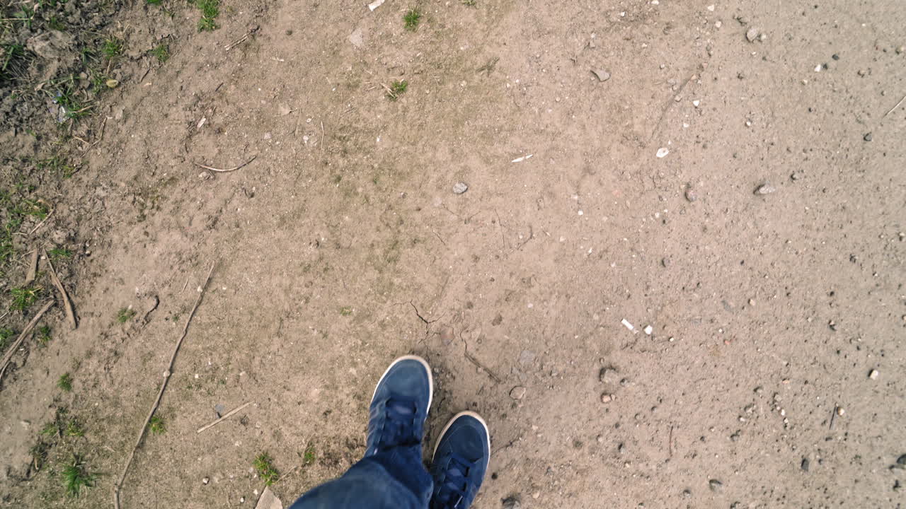 Male's legs going on the ground and a lot of garbage around outdoors. Man in jeans and trainers come into the dirty place with many rubbish on the natural background.