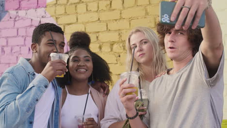 group of  young friends taking selfies together and having fun outdoors, while holding and drinking their fresh drinks in plastic cups