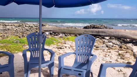 Tienda-De-Campaña-Al-Aire-Libre-En-La-Playa-De-Arena-Con-Sillas-Azules-Y-Viento,-Panorámica-A-La-Derecha