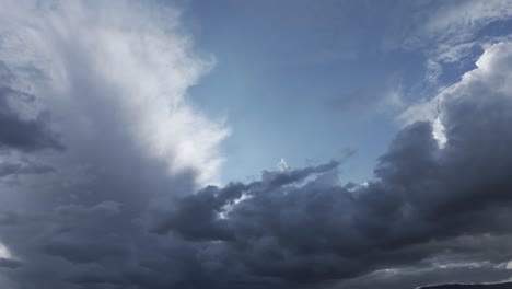 vuelo con un dron visualizando un cielo azul pero con grandes nubes agrupadas, posiblemente nubes de tormenta, vemos en detalle que el sol está escondido en una nube alargada, dándole mucha claridad en sus lados