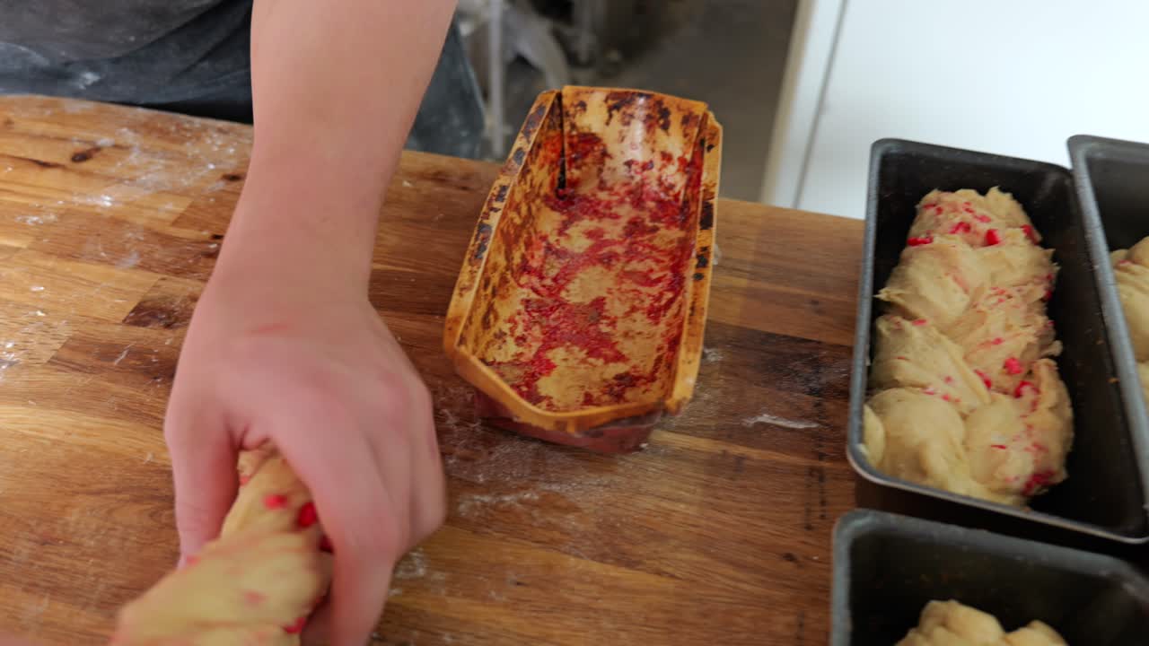 Un panettiere posiziona a mano un impasto intrecciato ripieno di praline in uno stampo di metallo.